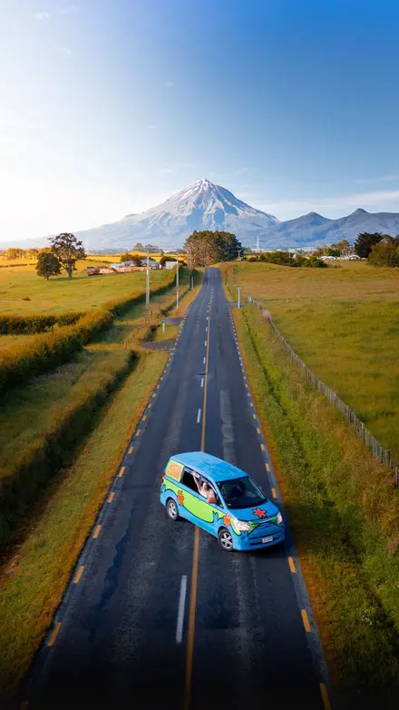 Aerial road trip view with a blue Wicked campervan driving toward Mount Taranaki