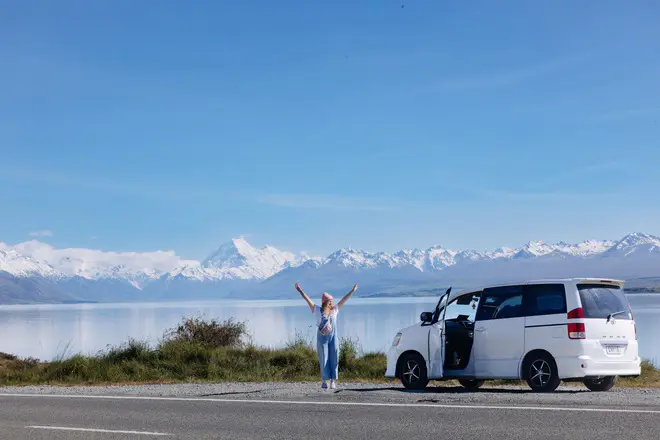 Traveller beside a white Wicked campervan with snowy Mount Cook views in New Zealand